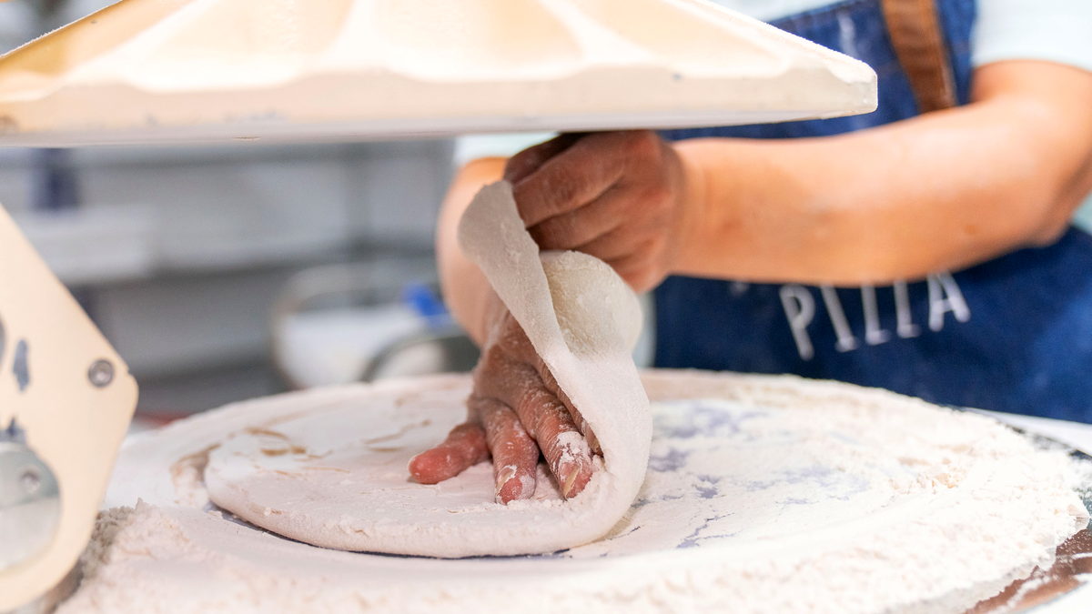 Pizzaiolo estirando a mano una masa de fermentación natural en la fábrica IOLA
